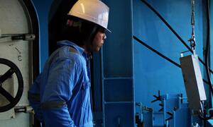 A seafarer wearing blue coveralls and a white safety helmet standing in a ship's engine room.