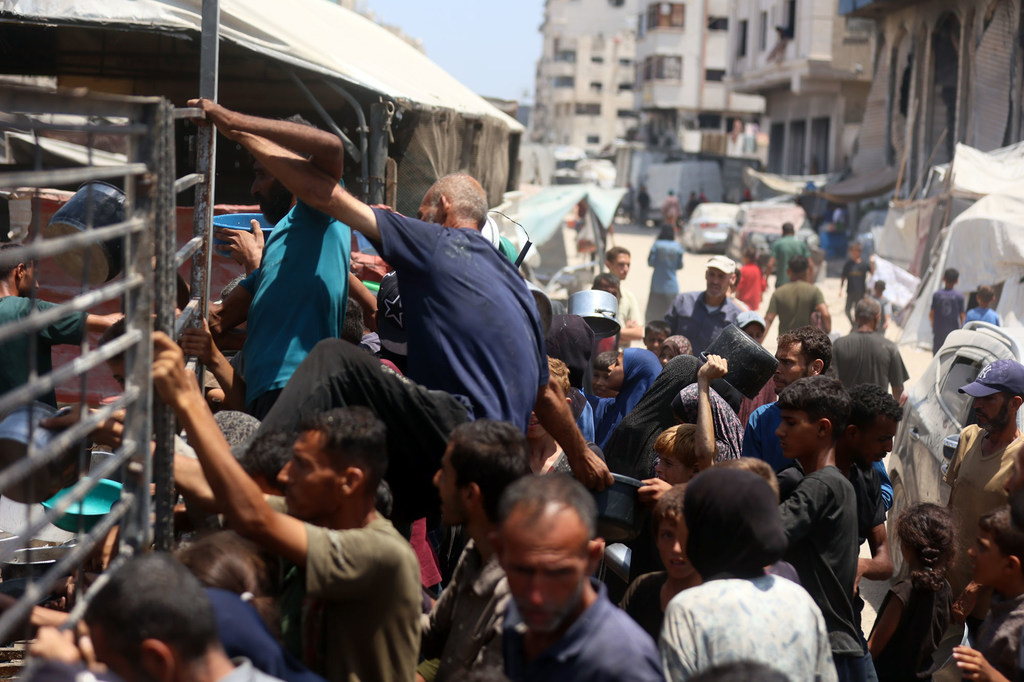 Hombres escalan las barreras de una cocina comunitaria en el oeste de la Ciudad de Gaza en busca de comida (foto de julio de 2025).