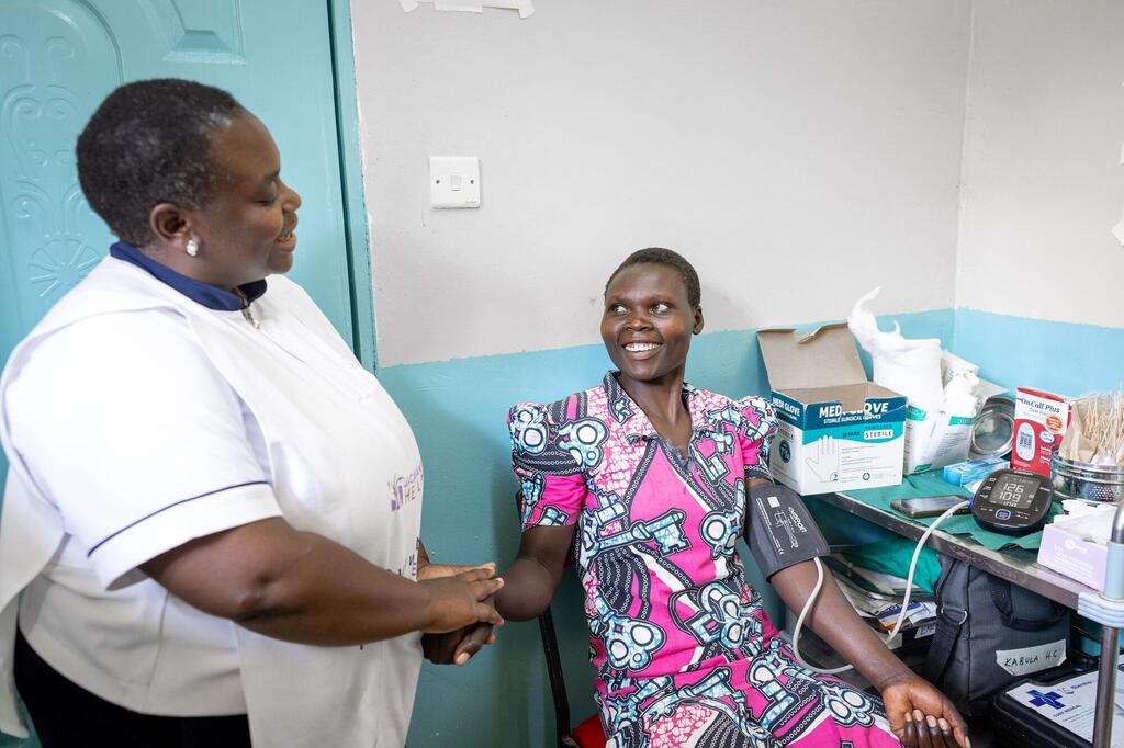 Mfanyakazi wa afya aliyevalia mavazi meupe anachunguza shinikizo la damu la mgonjwa mwenye tabasamu katika kliniki moja nchini Kenya.