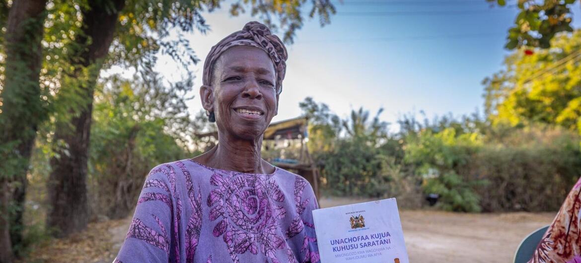 Une femme souriante au Kenya tenant une brochure de l'OMS sur le cancer du col de l'utérus.