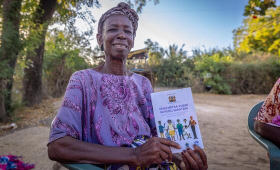 A smiling woman in Kenya holding a WHO cervical cancer awareness pamphlet.
