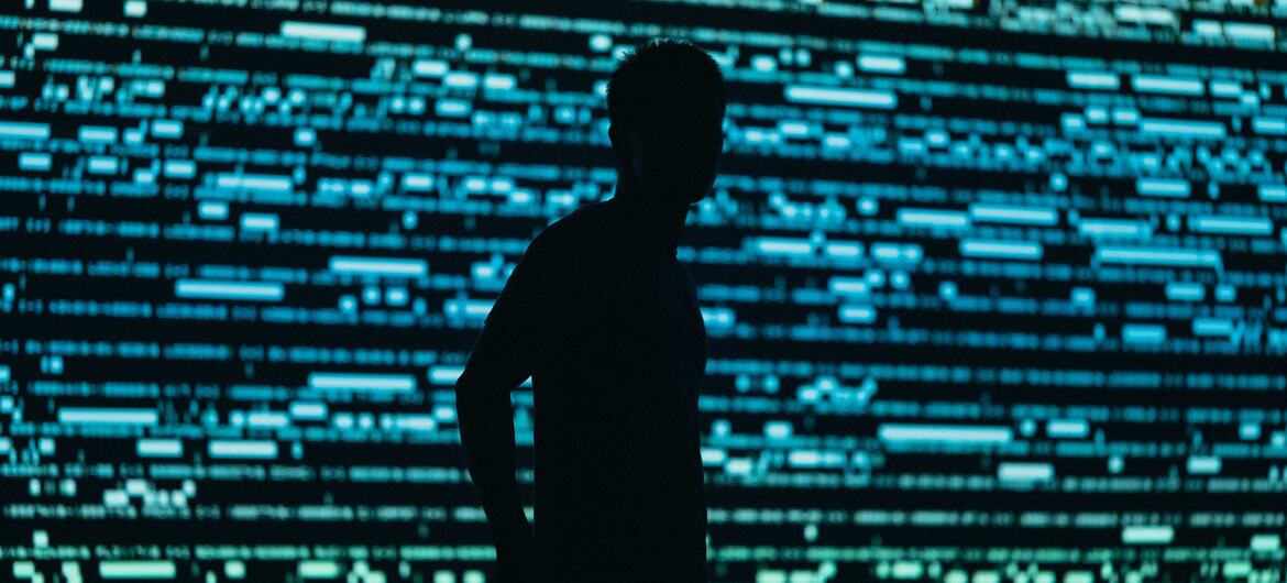 Una silueta de un hombre de pie frente a una pantalla digital de datos azul.