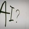 El texto escrito a mano en una superficie blanca dice 'AI?' con un signo de interrogación, que simboliza la curiosidad o la incertidumbre sobre la inteligencia artificial.