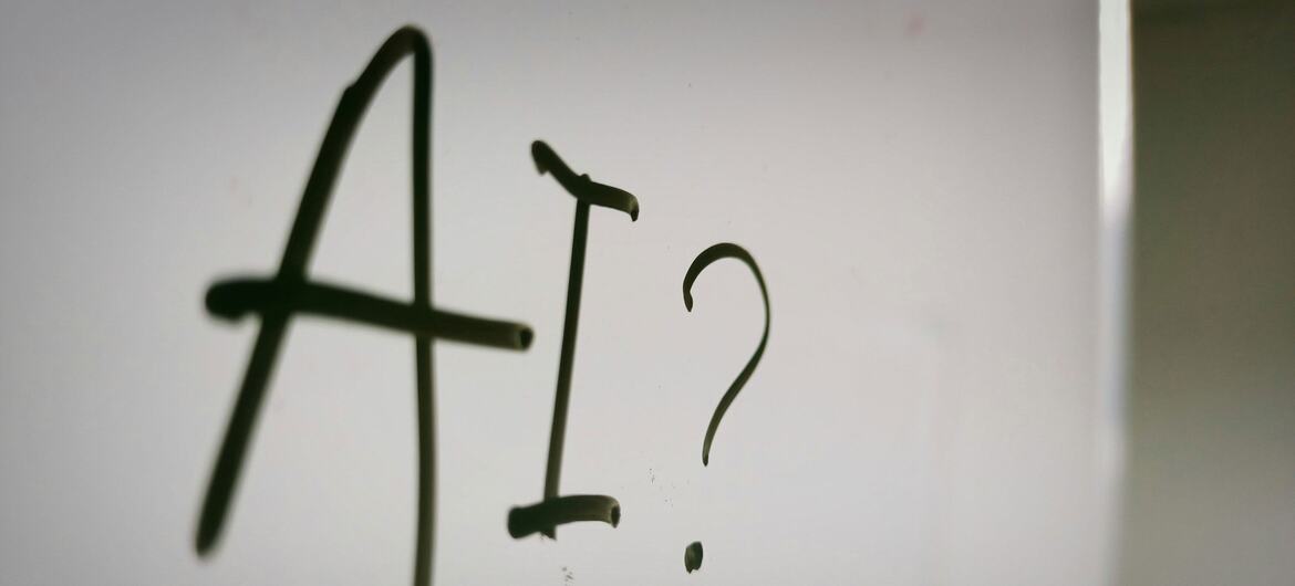 El texto escrito a mano en una superficie blanca dice 'AI?' con un signo de interrogación, que simboliza la curiosidad o la incertidumbre sobre la inteligencia artificial.