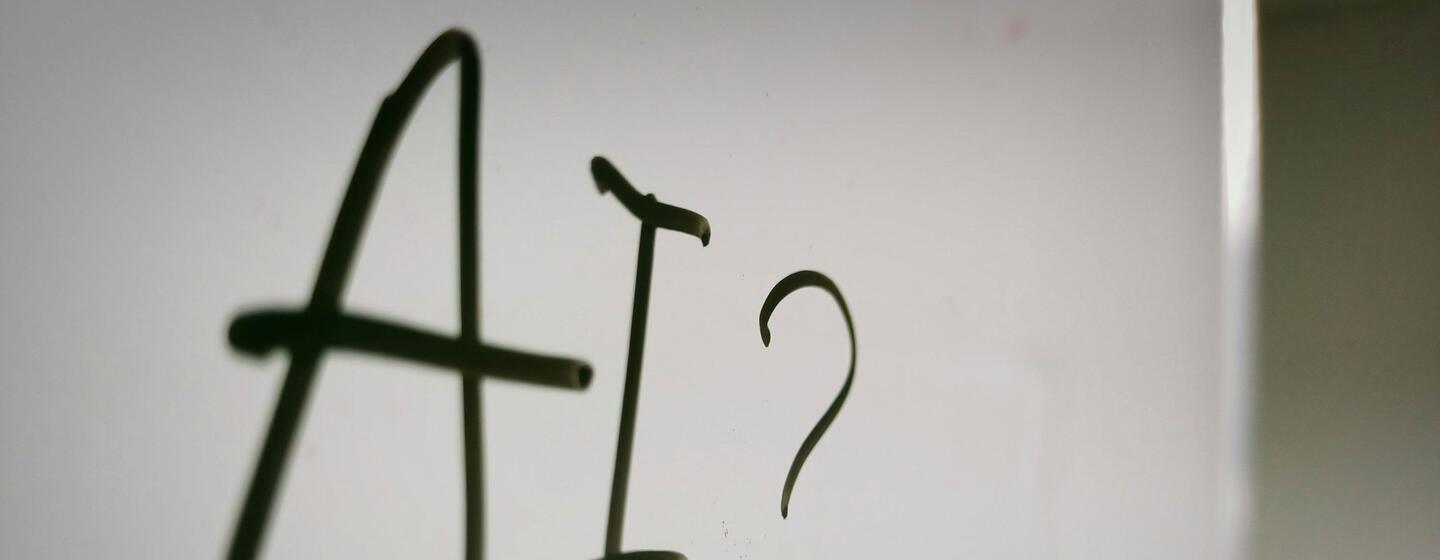 El texto escrito a mano en una superficie blanca dice 'AI?' con un signo de interrogación, que simboliza la curiosidad o la incertidumbre sobre la inteligencia artificial.