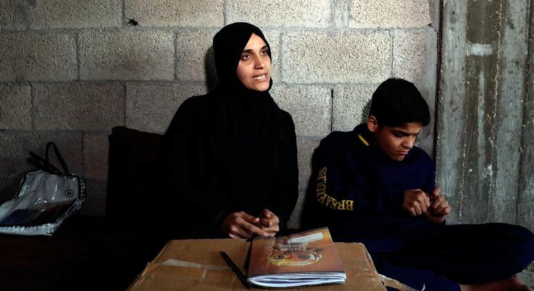 امرأة فلسطينية وصبي صغير مصاب بالتوحد يجلسان على مكتب مؤقت في غرفة بسيطة بها جدران من الكتل الرمادية، يركزان على المواد التعليمية.