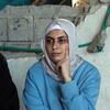 امرأة فلسطينية متأملة في حجاب تجلس أمام جدار متضرر في غزة.