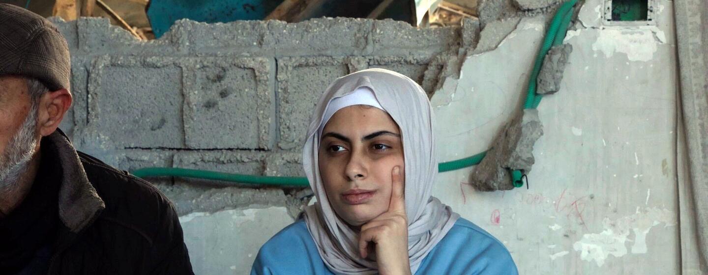 Una palestina contemplativa con hiyab se sienta frente a un muro dañado en Gaza.