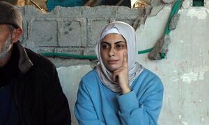 Una palestina contemplativa con hiyab se sienta frente a un muro dañado en Gaza.