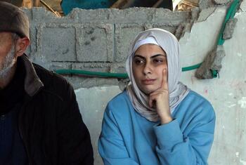 Una palestina contemplativa con hiyab se sienta frente a un muro dañado en Gaza.