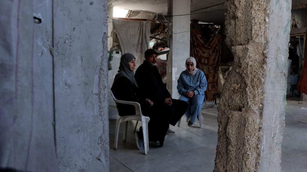 Una familia palestina se sienta dentro de un edificio dañado en Gaza, rodeada de escombros y destrucción.