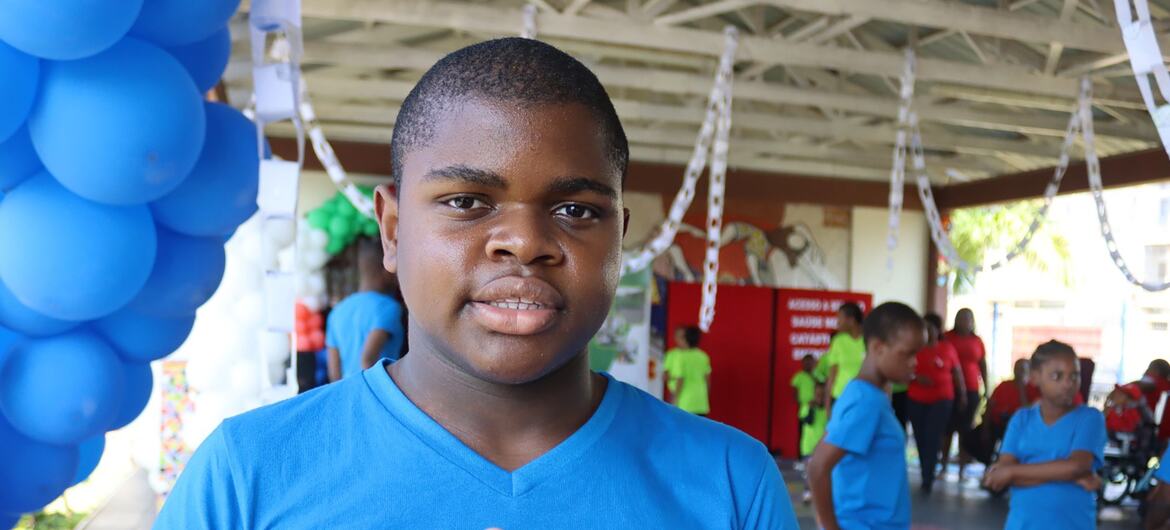 Um menino com autismo num evento em Lihimia, Moçambique, vestindo uma camisa azul e usando a linguagem gestual.