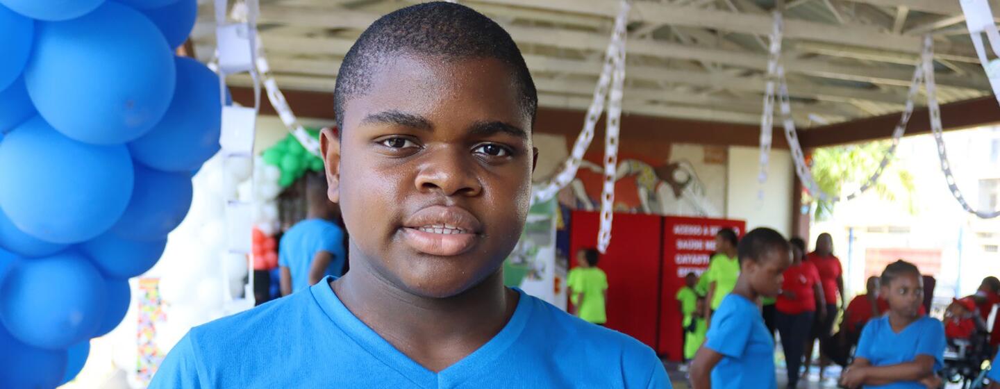 Um menino com autismo num evento em Lihimia, Moçambique, vestindo uma camisa azul e usando a linguagem gestual.