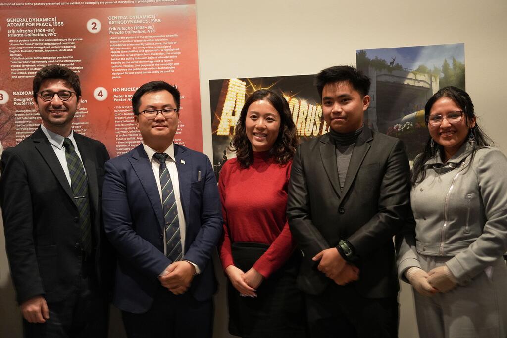 Five attendees of the Youth Leaders Fund stand together in front of a poster display at an exhibition on nuclear disarmament.