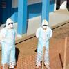 Two healthcare workers in protective gear stand outside a blue building under construction, enclosed by an orange safety fence in Bunia, DR Congo.