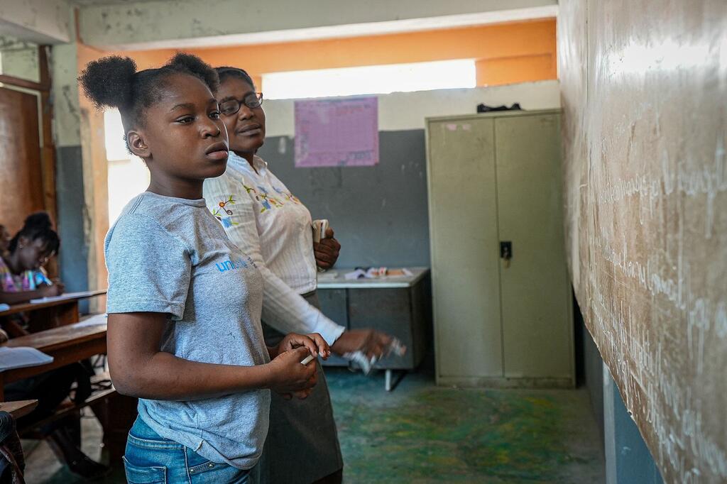 Dieussika, une enfant déplacée d'Haïti, se tient dans sa salle de classe vêtue d'une chemise de l'UNICEF, tenant une craie, et apparaît concentrée pendant qu'elle participe à un cours.