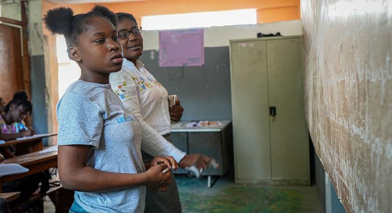 Диессика, беженка на Гаити, стоит в классе в футболке ЮНИСЕФ, держит крет и, участвуя в уроке, выглядит сосредоточенной.