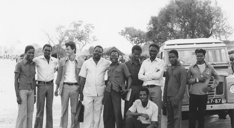Um grupo de homens, incluindo refugiados e trabalhadores humanitários, posando em frente a um veículo em um campo de refugiados em Moçambique.