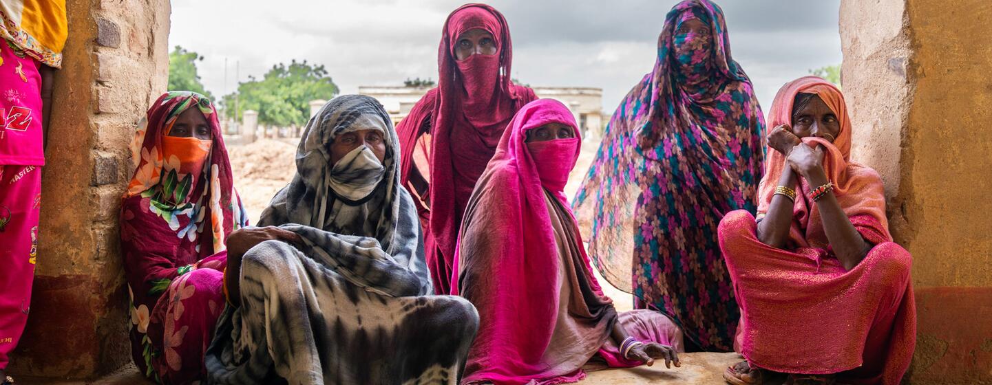 Un groupe de femmes et de filles portant des vêtements traditionnels colorés et des couvre-visages s'assoit à l'intérieur d'une structure simple, reflétant les défis auxquels sont confrontés les rapatriés au Soudan.