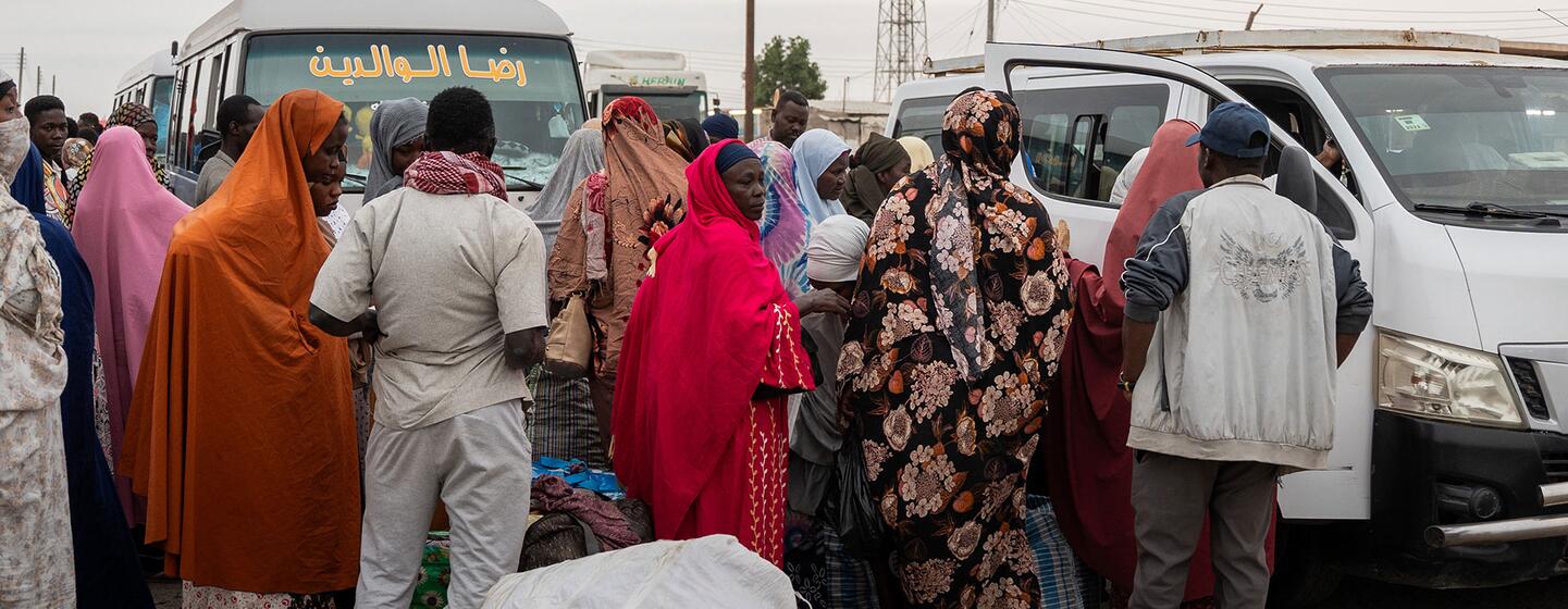Les rapatriés soudanais se tiennent avec leurs affaires près d'un bus et d'un minibus.