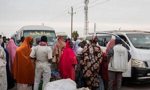 Les rapatriés soudanais se tiennent avec leurs affaires près d'un bus et d'un minibus.