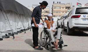 A patient in a wheelchair is being assisted by a staff member at Al-Amal Hospital in Gaza, affiliated with the Palestinian Red Crescent Society, preparing for transport. A UN vehicle is parked nearby.