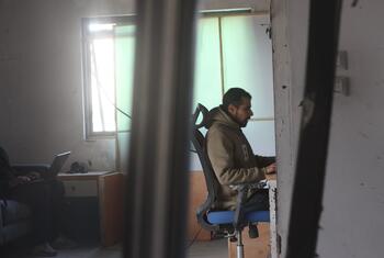 Un periodista trabaja en un escritorio en una oficina dañada en Gaza, visto a través de pilares rotos.