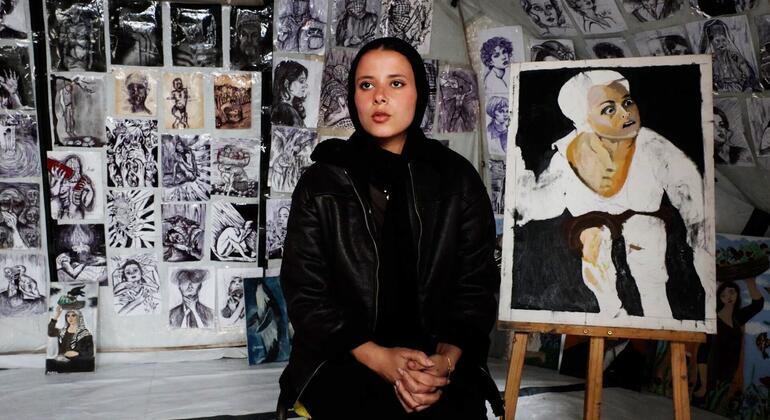 الفنانة الفلسطينية الشابة، فرح خالد تجلس أمام إحدى لوحاتها في الخيمة التي حولتها إلى معرض فني في قلب مدرسة تابعة لوكالة الأونروا التي تحولت إلى مركز لإيواء النازحين في مدينة غزة.