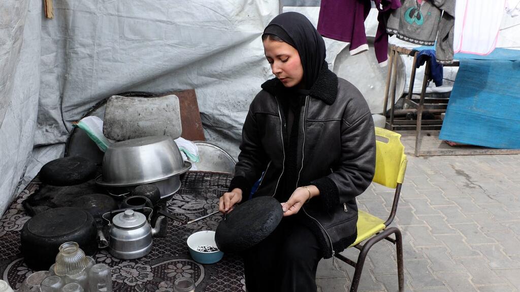 الفنانة الفلسطينية الشابة مرح خالد أثناء كشط السخام من أواني الطهي لاستخدامه في رسم لوحاتها.