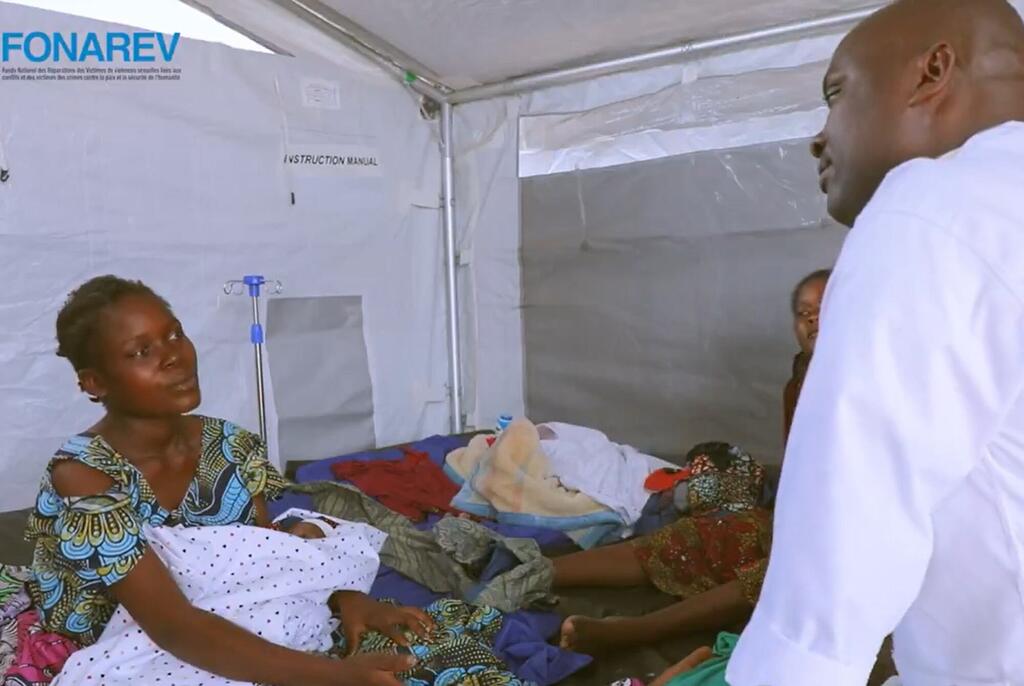 Mwanamke anayebeba mtoto mchanga katika hema la matibabu huko Busuma, Burundi, akizungumza na mhudumu wa afya.