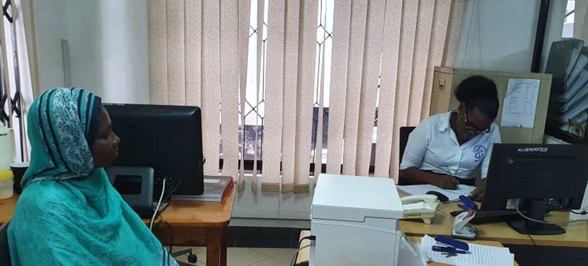 Wanawake wawili wanaofanya kazi katika mazingira ya ofisi nchini Tanzania, mmoja ameketi na kutazama kamera, mwingine amekazia kuandika kwenye dawati lake.