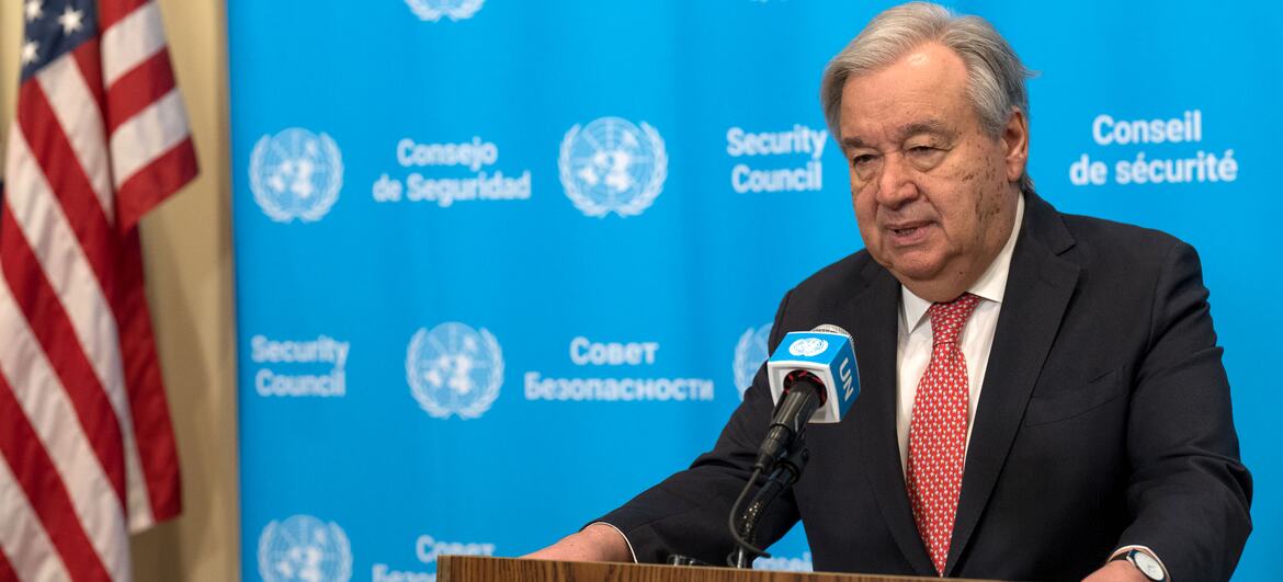 O secretário-geral das Nações Unidas, António Guterres, fala em um pódio durante uma conferência de imprensa no Conselho de Segurança da ONU, com bandeiras dos EUA e do Reino Unido visíveis.