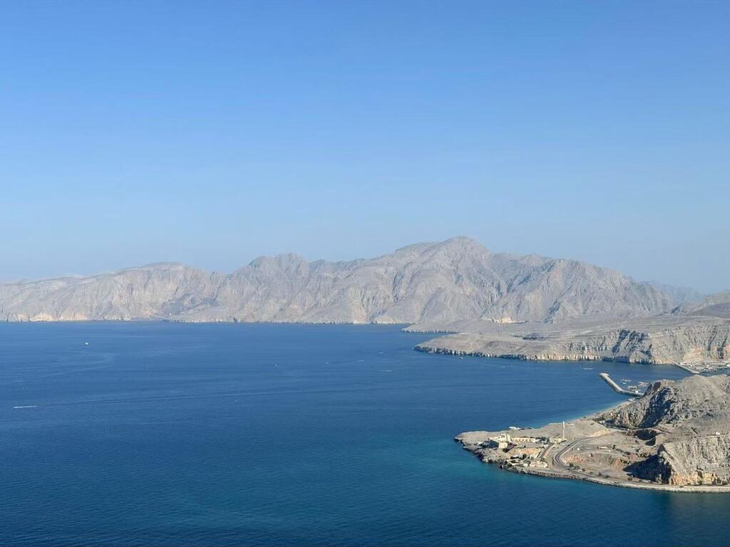 Una amplia bahía con aguas de un azul profundo, bordeada por montañas áridas y rocosas y un pequeño asentamiento costero a la derecha.