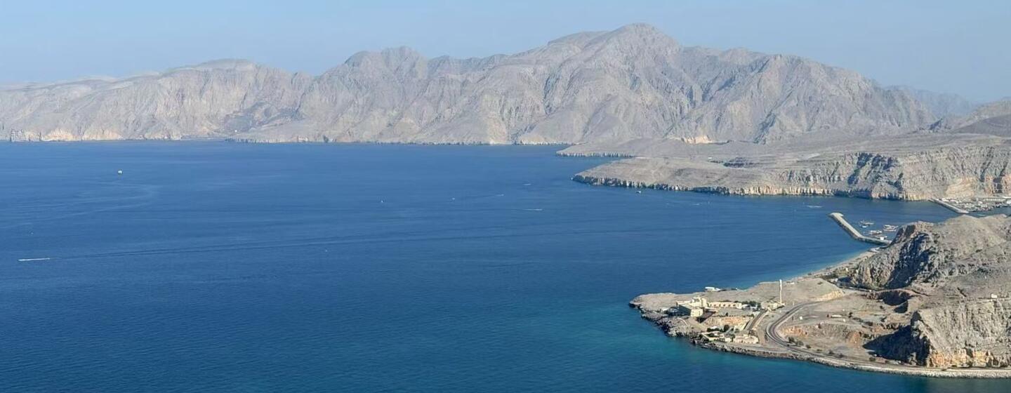 Une large baie aux eaux bleu profond, bordée par des montagnes rocheuses arides et une petite agglomération côtière à droite.