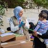 Mfanyakazi wa UNICEF aliyevalia hijab ya bluu nyepesi na koti, akiwa amevaa glavu za bluu, anapima ukuaji wa mtoto aliyebebwa na mama katika makao ya muda huko Beirut, Lebanoni.