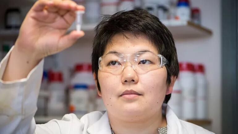 Une scientifique portant des lunettes de sécurité et un manteau de laboratoire tient un petit tube à essai dans un laboratoire.