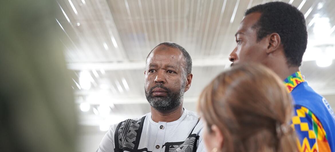 Mohammed Abdiker, um homem de barba com uma camisa de padrão branco, está numa discussão de grupo, olhando cuidadosamente para alguém fora da câmera.
