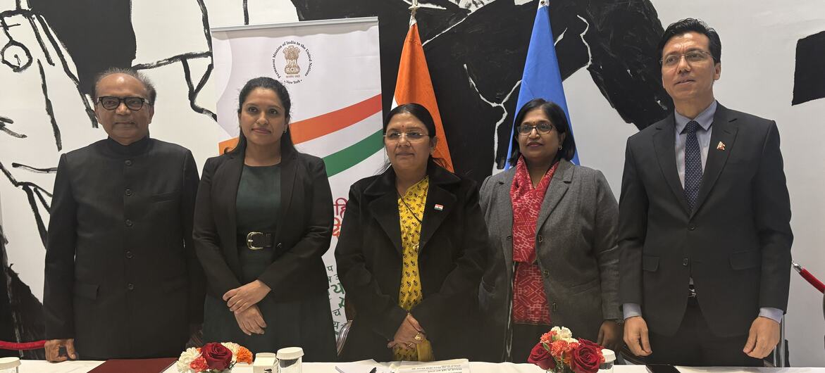 न्यूयॉर्क में एक हिंदी दिवस कार्यक्रम के दौरान पांच भारतीय राजनयिक एक सम्मेलन मेज पर खड़े हैं, पृष्ठभूमि में नाम प्लेट और राष्ट्रीय ध्वज हैं।