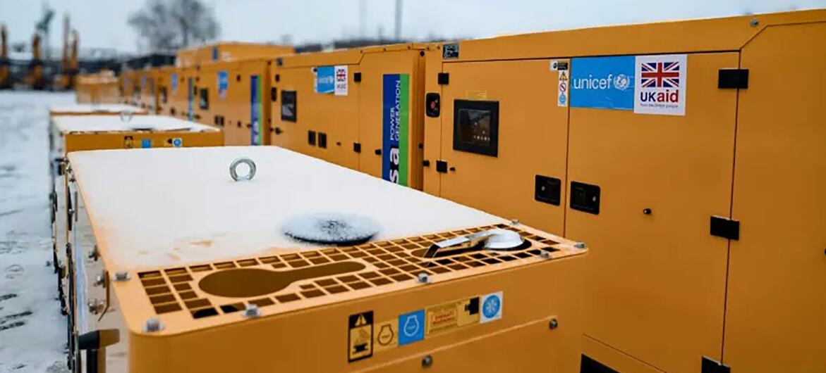 Une rangée de générateurs électriques jaunes recouverts de neige, marqués avec des logos d'aide de l'UNICEF et du Royaume-Uni, placés sur un fond d'hiver en Ukraine.