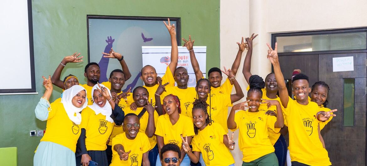 A group of smiling youth in yellow t-shirts with handprint logos pose enthusiastically at an UNFPA Kenya FGM eradication campaign event.