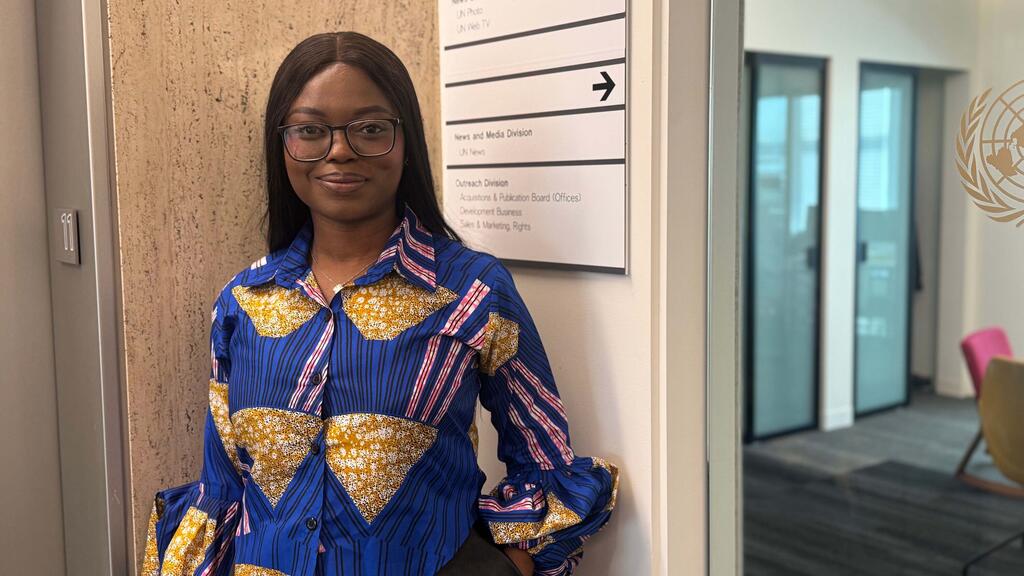 Picha ya mwanaharakati wa haki za binadamu wa Nigeria akiwa amesimama katika ukumbi wa ofisi karibu na ishara ya Idara ya Habari na Vyombo vya Habari ya Umoja wa Mataifa, na nembo ya Umoja wa Mataifa ikionekana ukutani.