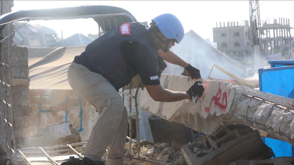 Un trabajador de la UNMAS con casco azul y chaleco de seguridad marca un trozo de escombros en Gaza.