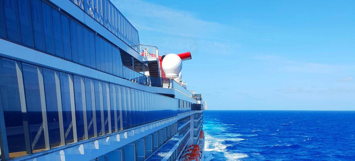 Vue latérale d'un grand navire de croisière naviguant sur un océan bleu, montrant son sillage.