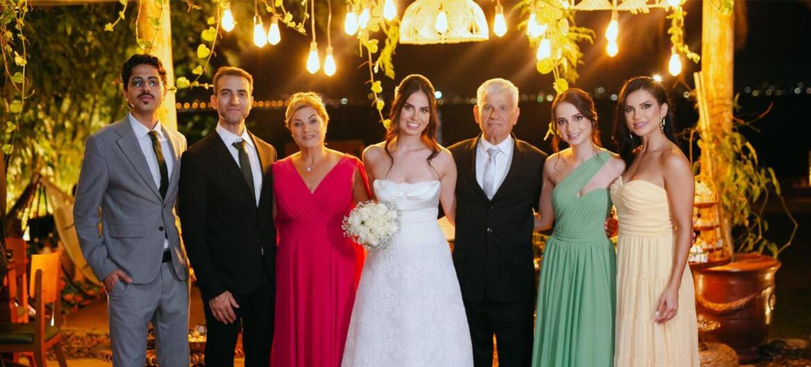 Uma noiva e um noivo posam com seu grupo de casamento em um evento noturno ao ar livre com luzes de corda.