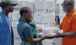 Mfanyakazi wa misaada wa UNFPA anamkabidhi mwanamke mmoja mkimbizi katika Burundi vifaa vya kutoa misaada, akiwa na vifurushi vya misaada katika mandhari ya nyuma.