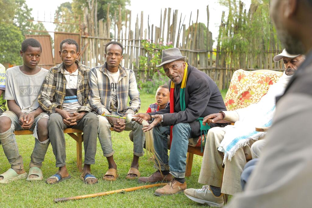 Un grupo de hombres, incluido un hombre mayor, se sientan juntos al aire libre en un entorno comunitario, simbolizando la resistencia contra la mutilación genital femenina en Etiopía.