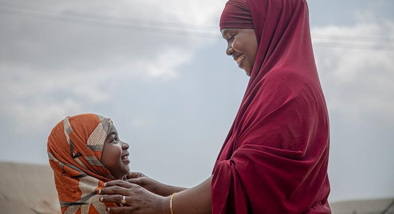 ریڈ ہیڈ سکارف پہنے ایک خاتون اورنج ہیڈ سکارف پہنے ایک نوجوان لڑکی کے سر کو ہلکے سے چھو رہی ہے۔ دونوں ایک دوسرے کی طرف دیکھتے ہوئے مسکرا رہے ہیں۔ یہ تصویر صومالیہ میں خواتین کے عضو تناسل کے منقطع ہونے کے خلاف لچک اور کمیونٹی مزاحمت کی علامت ہے۔