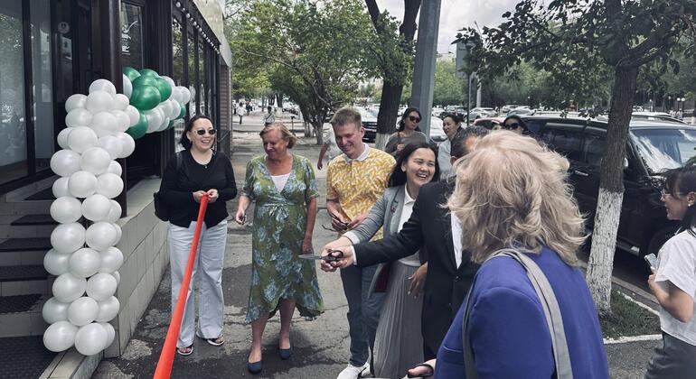 Группа людей участвует в церемонии резки ленты за пределами здания, украшенного белыми и зелеными воздушными шарами.