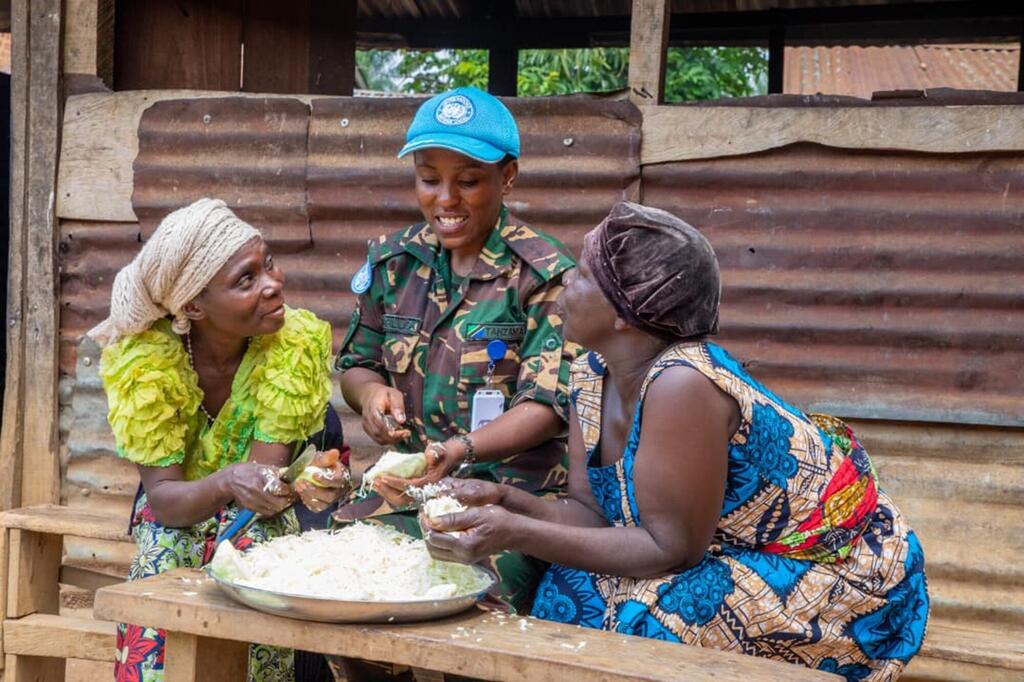Un pacificateur tanzanien de l'ONU en uniforme interagit chaleureusement avec deux femmes locales alors qu'elles partagent un repas ensemble à l'extérieur.