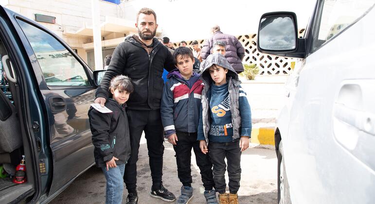 والد يدعى عمر يقف مع أطفاله الثلاثة عند معبر جدة يابوس الحدودي إلى الجمهورية العربية السورية، محاط بالمركبات.